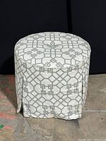 Front view of round upholstered ottoman with grey geometric pattern on white fabric upholstery on side and top. Shows overall shape and pattern.