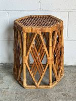 Front-left angled view of vintage hexagonal rattan table with woven top and diamond sides, showing natural finish and wear.