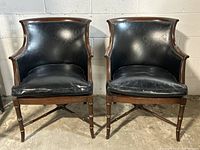 Front view of two black leather vintage lounge chairs showing wooden frames with stud detailing and black leather cushions.