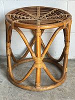 Front view of vintage natural rattan stool showing lattice weave top and round frame with rattan bindings.