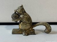 Side angle of vintage brass squirrel figurine holding a large acorn, showing textured tail and detailed fur etching