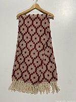 Rust and cream patterned throw blanket hanging on a wooden hanger against a white background.