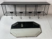 Front view of black wire hanging rack with five hooks and a rectangular etched wall mirror below it, both laid flat on a white surface.