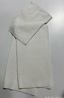 Folded white quilted pillow sham on top of another folded piece of fabric, showing texture and quilting detail