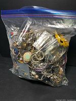Clear plastic zip-lock bag filled with various metal jewelry parts and pieces including earrings, rings, chains, and pendants.