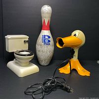 Photo showing the Crazy Duck hair dryer, toilet piggy bank, and Brunswick bowling pin from front view with power cord visible.