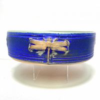 Side view showing the blue exterior glaze and embossed natural clay dragonfly motif on the round pottery dish.