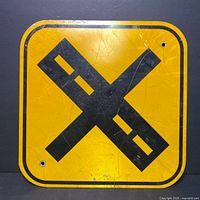Front view of the square yellow road sign with black railroad crossing 'X' symbol showing scratches and wear.