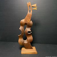 Front view showing the abstract contours and open spaces of the teak wood sculpture against a plain black background.