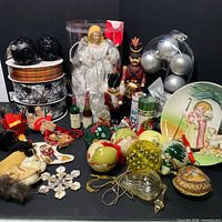 Overview of holiday ornaments and decor including Christmas tree ornaments, nutcracker figurine, angel tree topper, decorative plate, miniature bottles, and boxed ribbons.