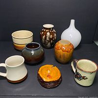 Photo showing six ceramic pieces including planters, mugs, and a white vase, plus one tree slice shaped handmade ashtray.