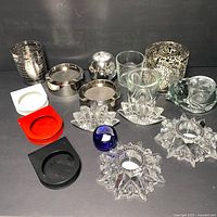 Various candle holders arranged on a black surface including crystal, metal, clear glass, and colored glass/plastic holders.