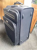 Side view of the large black softside suitcase showing wheels, feet and handle.