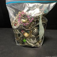 Small ziplock bag filled with mixed earrings, beads, hoop earrings, and assorted jewelry parts seen within.