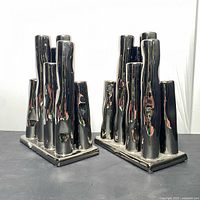 Pair of ceramic vases with tubular vertical elements and chrome paint finish, positioned side by side on a dark surface.
