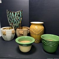 Front view of the lot of 6 assorted ceramic planters arranged against black background showing details and colors of each planter