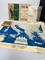 Vintage ephemera lot displayed including the 1943 CFAC Invasion Map of Europe showing Mediterranean Sea, Italy, Greece and surrounding areas, plus a green booklet on prairie weeds, and other war and Alberta maps.