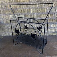 Front view of black metal vintage magazine rack showing the circular leaf design and textured base.