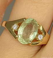 Close-up image of a yellow gold ring with an oval light green Zultanite gemstone and two small diamonds on each side.
