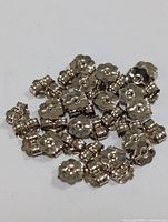 Pile of small 10K white gold earring backs with flower-shape, showing front and side details.