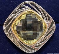 Close-up photo of square-shaped ring with large faceted lemon topaz gemstone in brass setting showing detailed geometric engraving on the brass bezel.