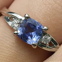 close-up of ring on finger showing cushion-cut blue tanzanite flanked by two small diamonds and split shank design