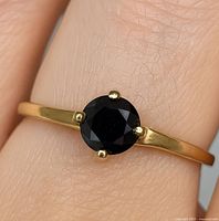 Close-up image of the ring worn on finger showing gold band and round black diamond.