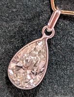 Close-up view of pear-shaped diamond and white gold bezel setting against dark background.