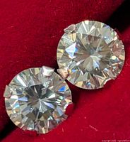 Close-up of two round moissanite stones in four-prong 10K gold settings on red velvet background.
