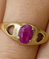 Close-up photo of the 10K gold ring on a finger showing the oval ruby set with heart-shaped cut-outs on the band sides.
