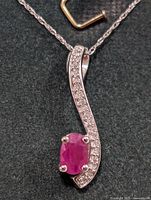 Close-up view of the pendant showing the oval ruby and diamonds on curved 10K gold setting.
