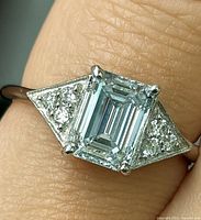 Top view of ring on finger showing emerald-cut center stone and side diamonds