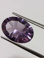 Faceted oval cut amethyst gemstone held by tweezers showing purple color and internal clarity details
