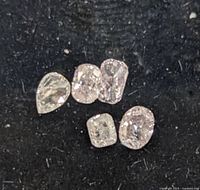 Five loose genuine diamonds of various shapes on black felt surface.