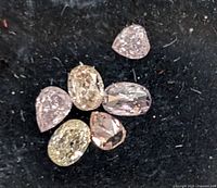 Close-up photo of six loose diamonds of mixed shapes and colors on black backing
