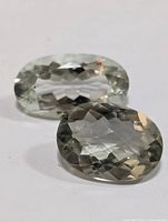 Photo showing two oval faceted green amethyst gemstones with light green translucent color on a white background.
