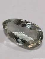 Pear-shaped faceted genuine green amethyst gemstone captured against white background, highlighting facets and clarity from side view.