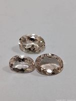 Three oval faceted morganite gemstones arranged in a triangular formation on a white background, showing color and clarity.
