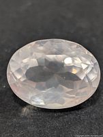 Close-up front view of oval faceted rose quartz gemstone on black background showing pale pink translucent color and faceting.