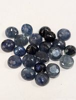 Collection of roughly 20 round faceted sapphire gemstones in blue hues.