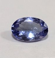 Close-up photo of an oval faceted blue-violet tanzanite gemstone showing transparency and internal inclusions.