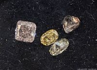 Close-up of four loose natural diamonds on black background showing various colors and cuts