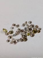 Multiple loose natural fancy color diamonds scattered on a white surface, showing front and back sides of the stones.