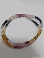 Full view of the faceted multi-color sapphire bead necklace laid in a circular shape showing the color distribution from dark blue to pink, yellow to green beads.