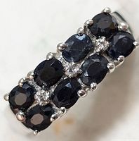 Close-up of silver ring with two rows of dark sapphire stones with clear accent stones in between, prong set.