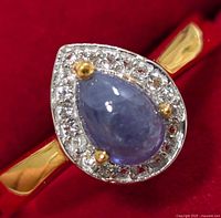 Close-up view of the ring showing tanzanite stone with halo of clear stones and gold prongs on a silver band.