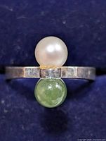 Close-up top view of silver ring with white pearl and green gemstone on blue background