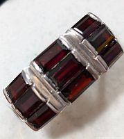 Close-up view showing the wide silver band with three rows of rectangular faceted garnet stones, polished silver between stones.