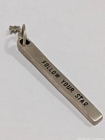 Close-up photo of rectangular sterling silver pendant engraved with 'FOLLOW YOUR STAR' and small star charm attached at top.