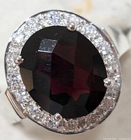Close-up top view of the oval garnet-colored faceted cubic zirconia center stone surrounded by clear CZ stones in a sterling silver setting.